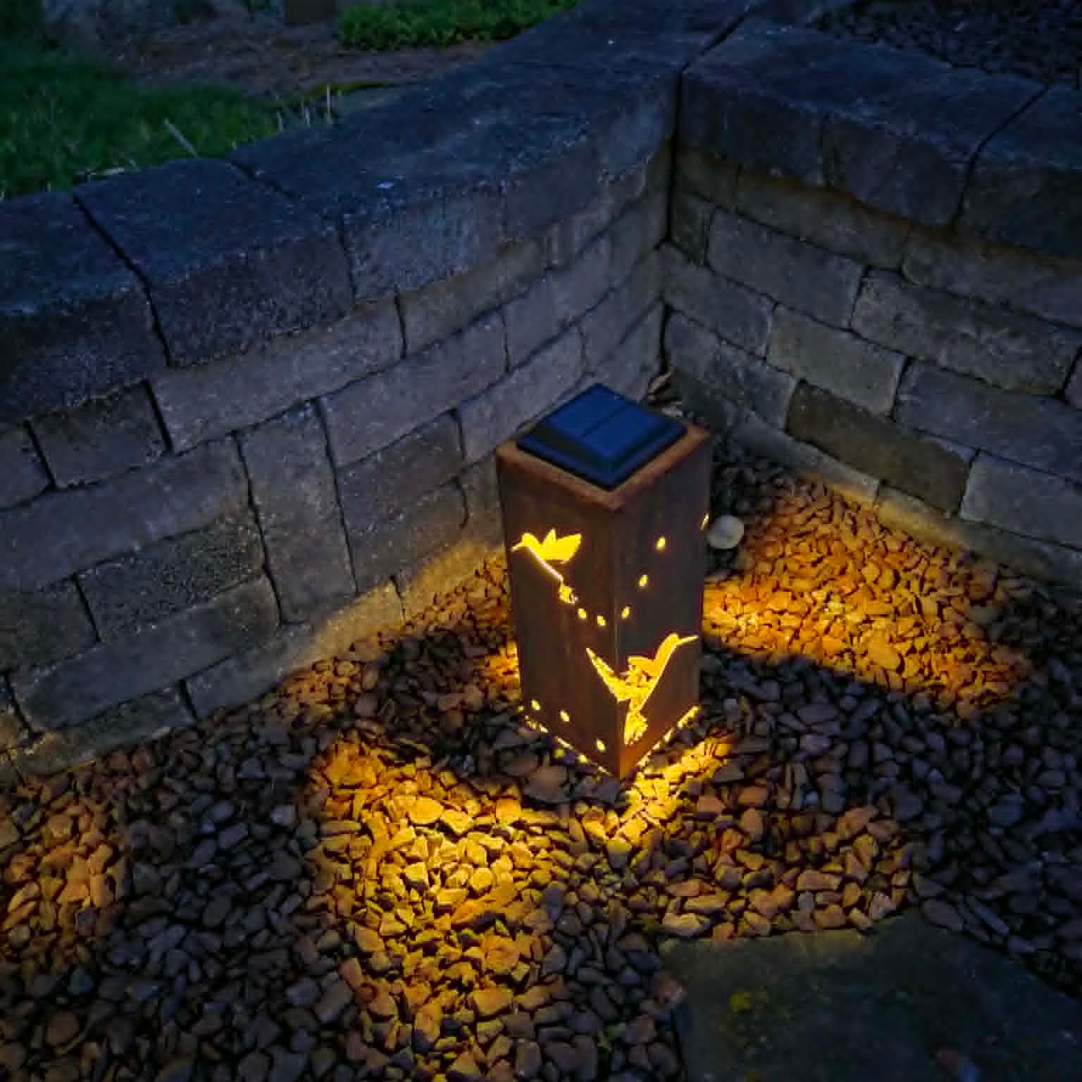 Solar-powered outdoor light fixture on pebbles near a stone wall