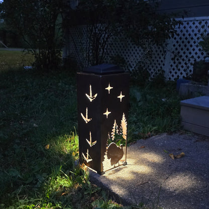 Rustic metal turkey solar pillar showing two sides glowing at dusk on front patio