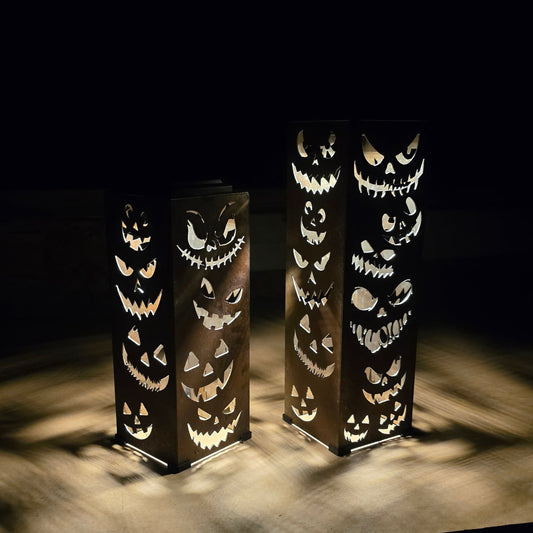 Two tall rectangular black lanterns with carved jack-o'-lantern cutouts, glowing from within on a dark surface against a black background.