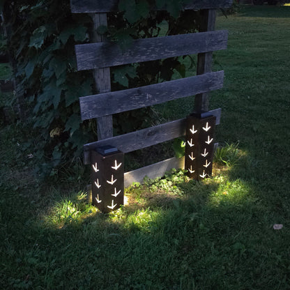 Rustic metal solar pillars with turkey prints on them glowing at dusk in front of a grape vine
