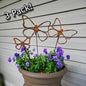 Three rusted metal butterfly decorative elements with a pot of purple flowers against a wooden background.