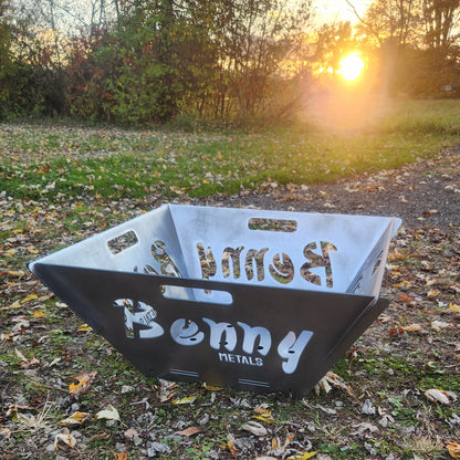 Flat pack fire pit with custom name sitting on ground with sunset