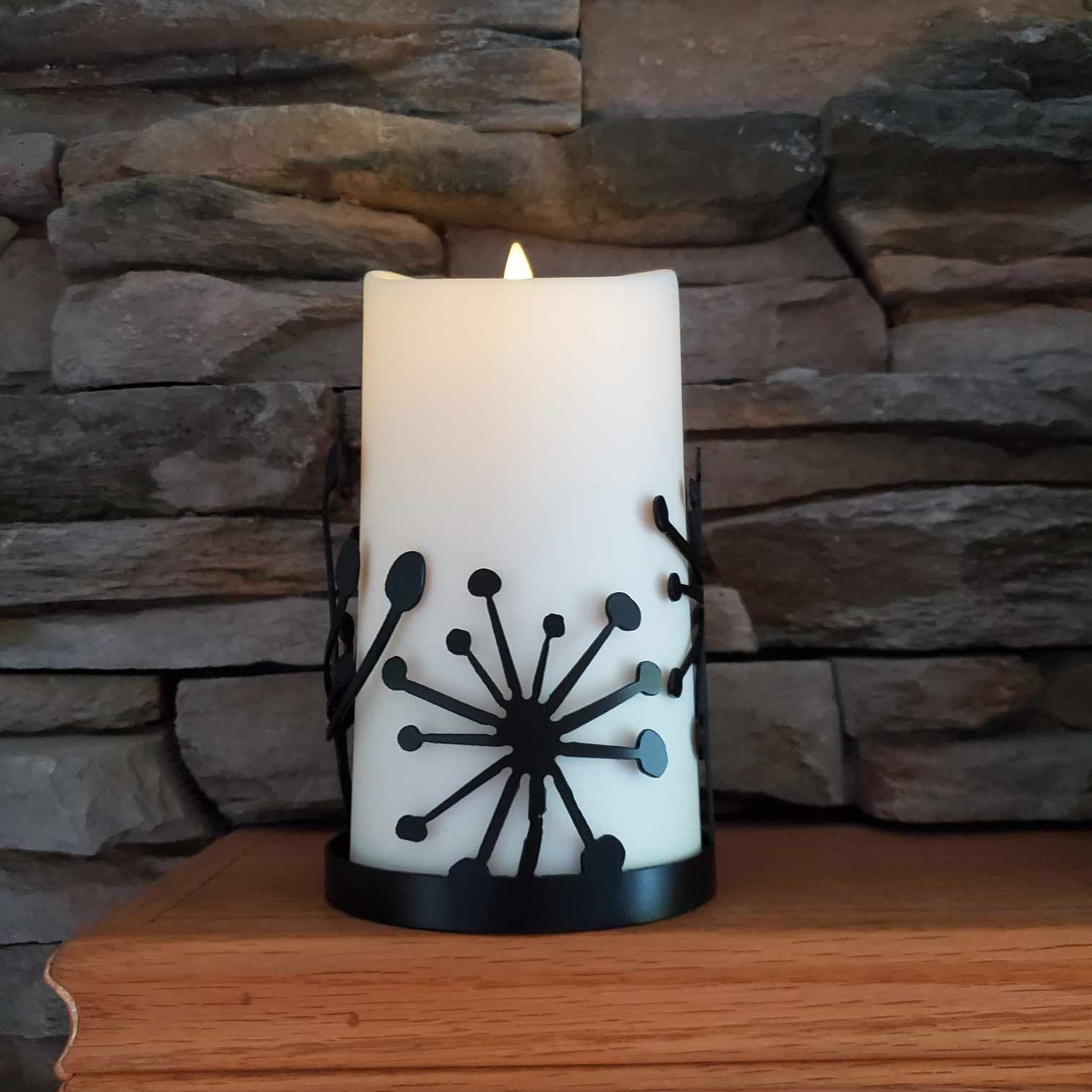 Black powder coated metal candle wrap with dandelions on it.