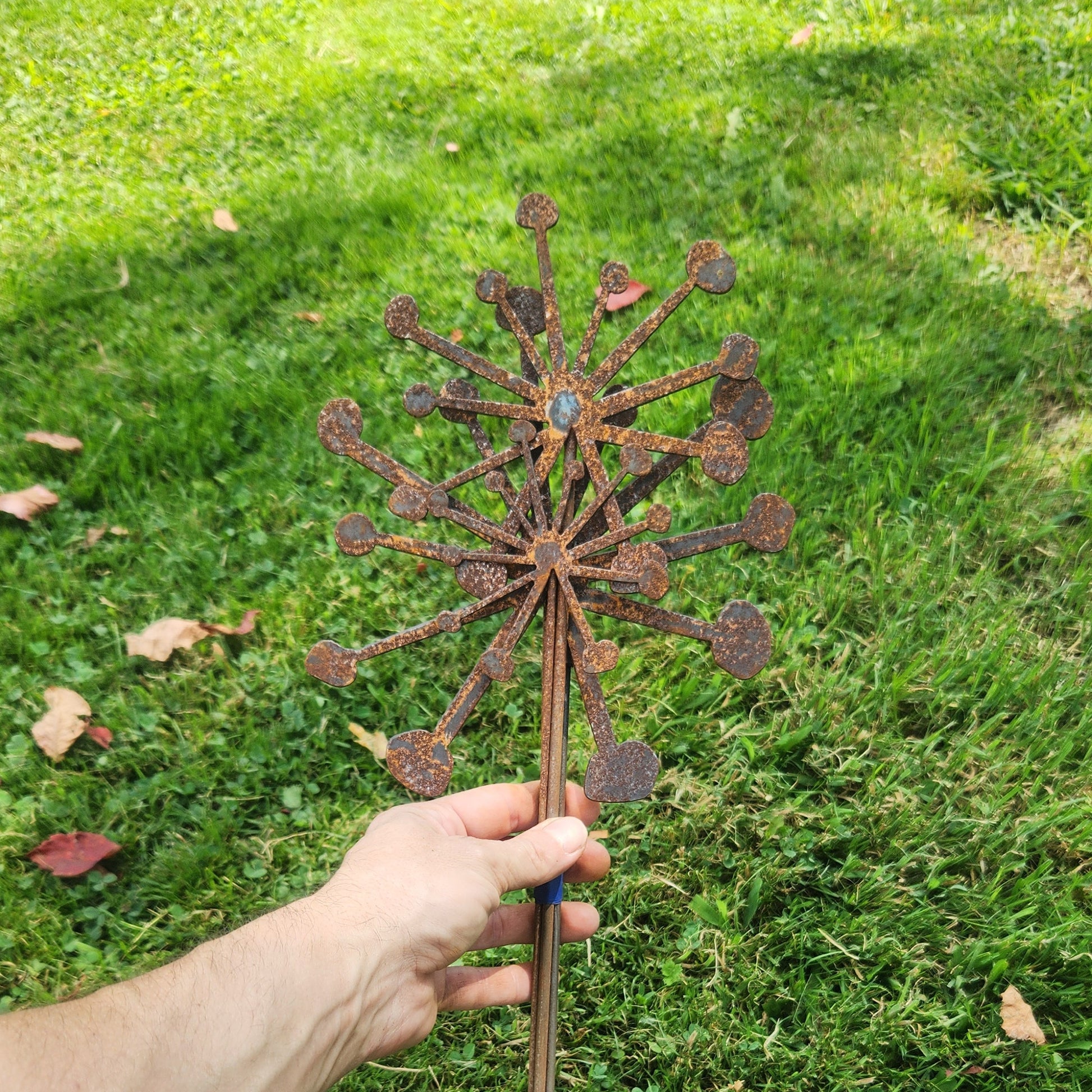 Hand holding a decorative metal garden stake against a grassy background