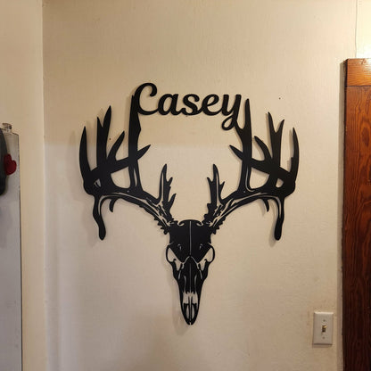 Decorative wall art of a deer skull with antlers and 'Casey' on a plain wall.