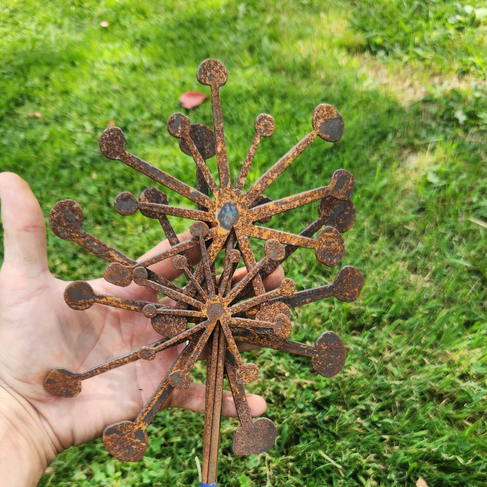 Metal decorative object resembling a flower held in a hand against a grassy background