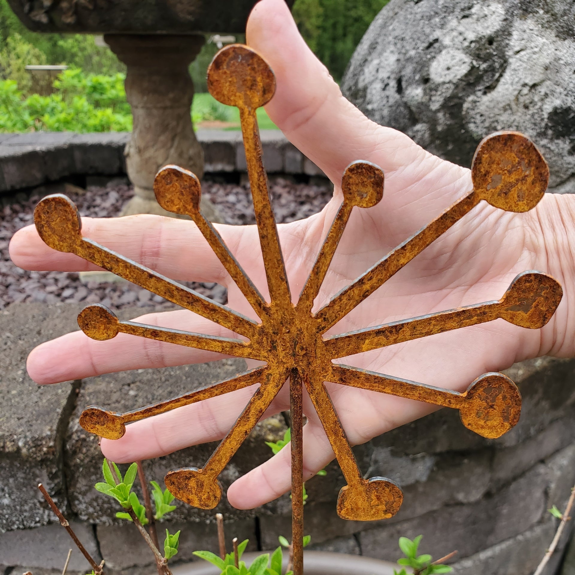 Rust-colored metal garden stake held by a hand with a garden background