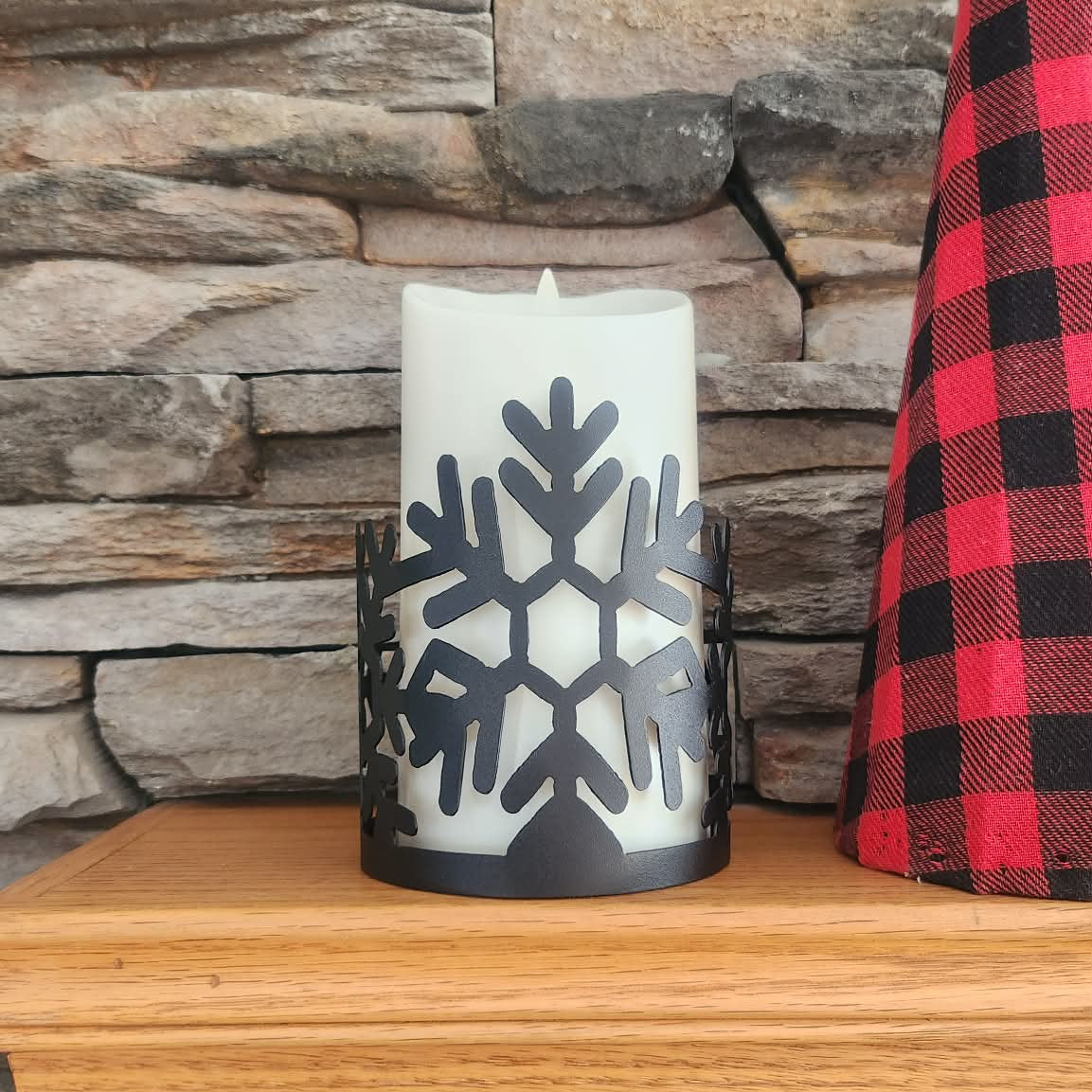Candle with snowflake design on a wooden surface against a stone wall background