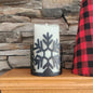 Candle with snowflake design on a wooden surface against a stone wall background