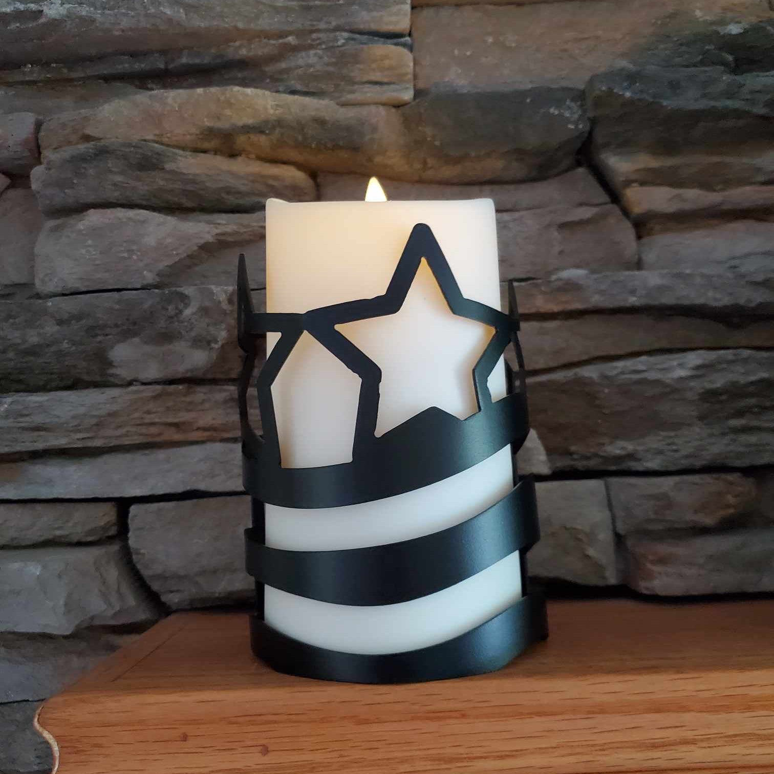 White candle with black star design on a wooden surface against a stone wall.
