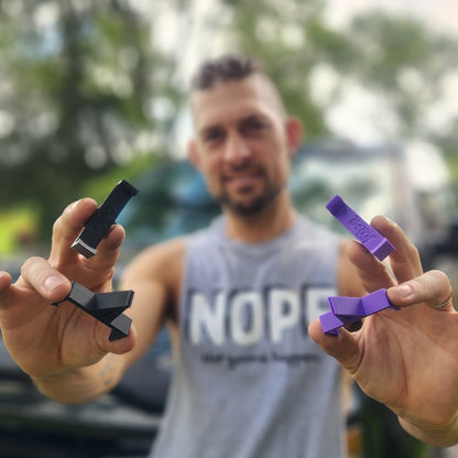 Man holding two small devices, one black and one purple, with a blurred background.