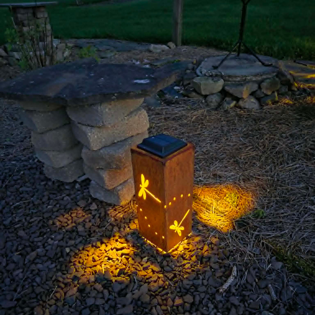 Solar-powered lantern with dragonfly design on a stone surface at night.