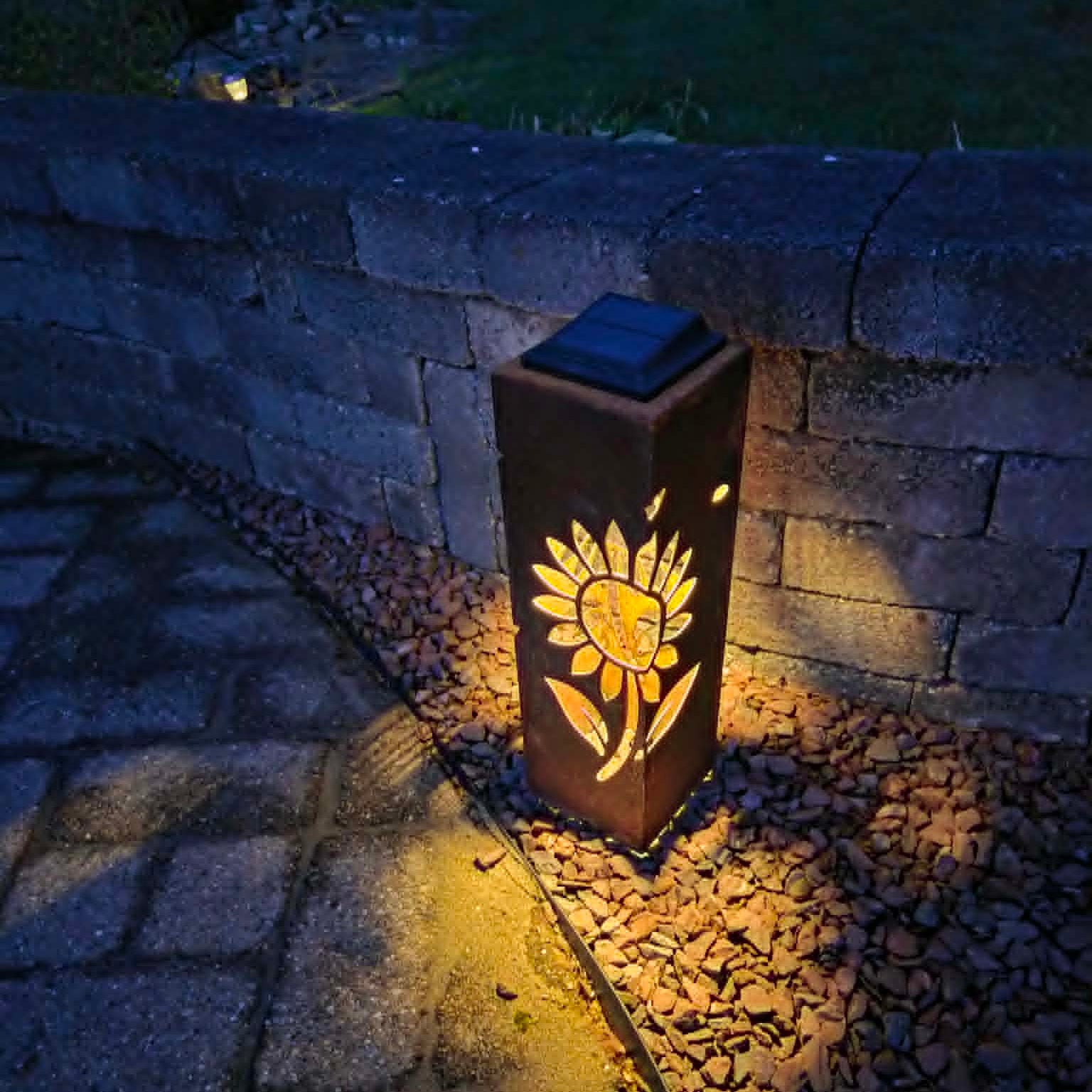 Solar-powered outdoor light with sunflower design on a stone pathway